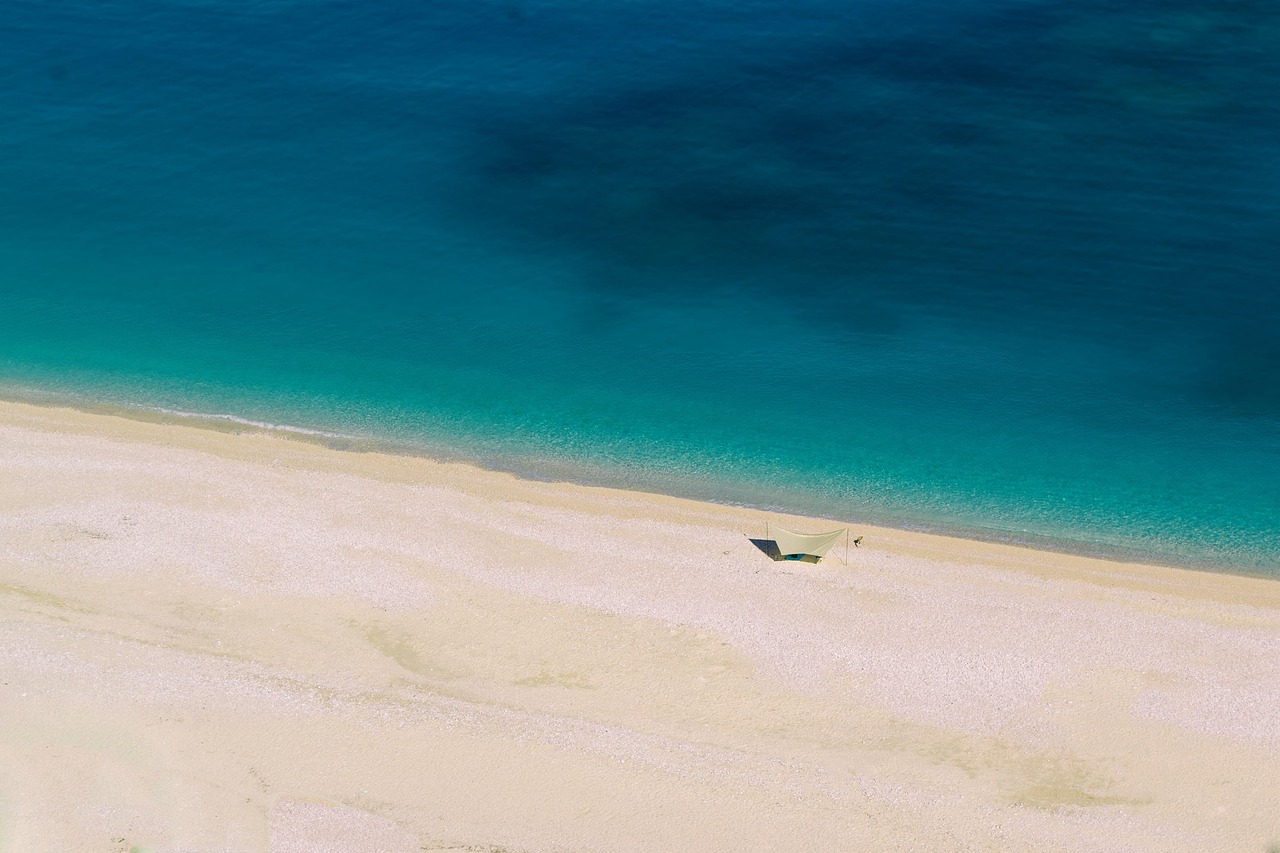 Spiaggia sabbiosa in Albania con acque cristalline e scogliere verdi sullo sfondo.