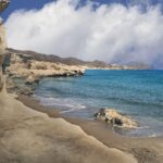 Vista panoramica di una spiaggia cristallina nell'arcipelago delle Cicladi, con sabbia bianca e acque turchesi.