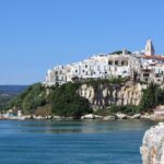Vista panoramica del borgo di Sperlonga con case bianche e la villa di Tiberio sullo sfondo del mare.