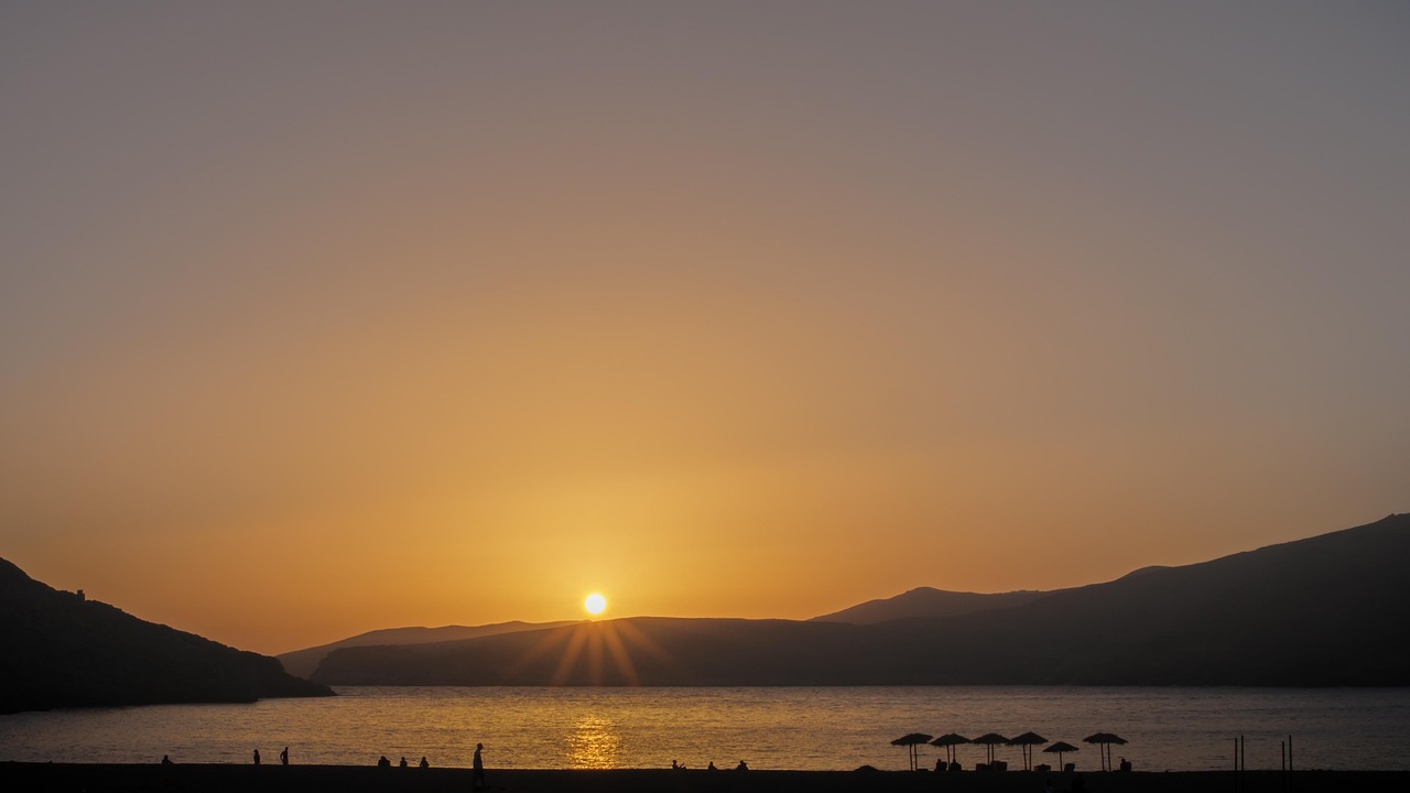Spiaggia greca con acqua cristallina e un romantico tramonto sullo sfondo.